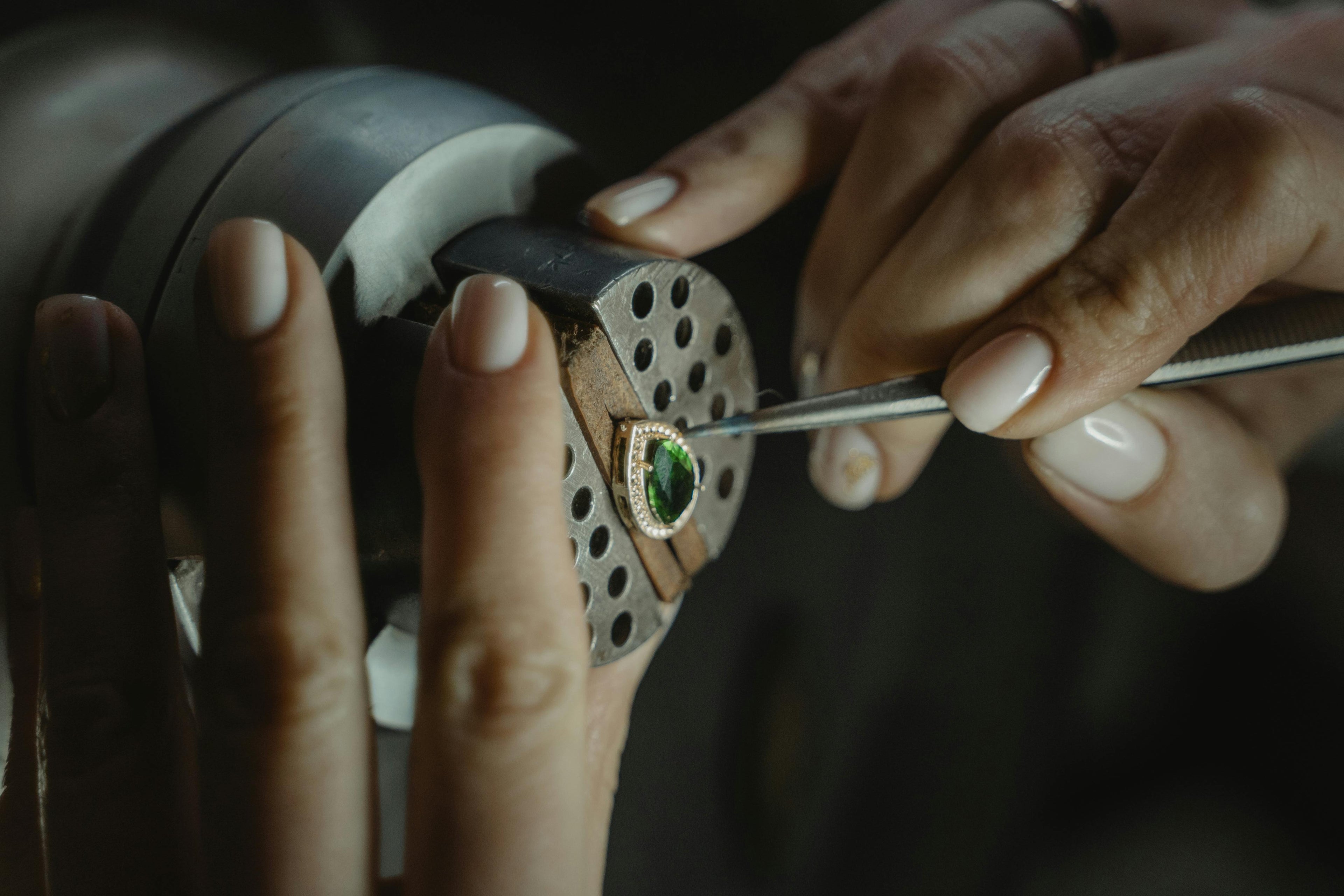 Stone setter's hands working on an emerald and diamonds pear shaped jewel.