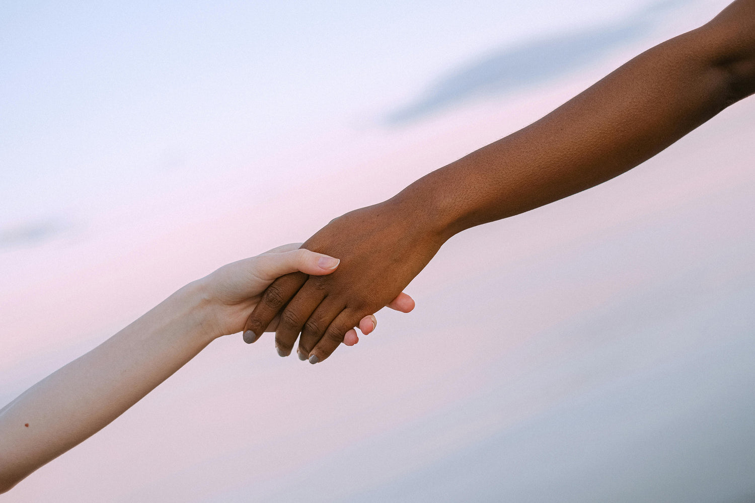 Two hands, one white and one black, reaching towards each other against a blurred background.