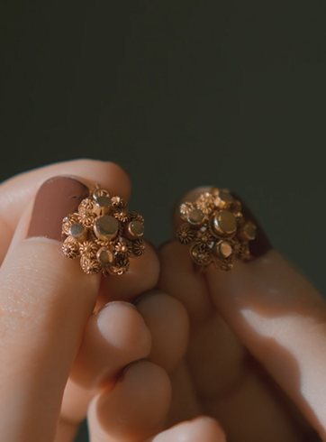 Gold earrings held between fingers against a dark background