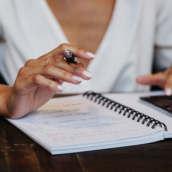 Person holding a pen over a notebook on a wooden table