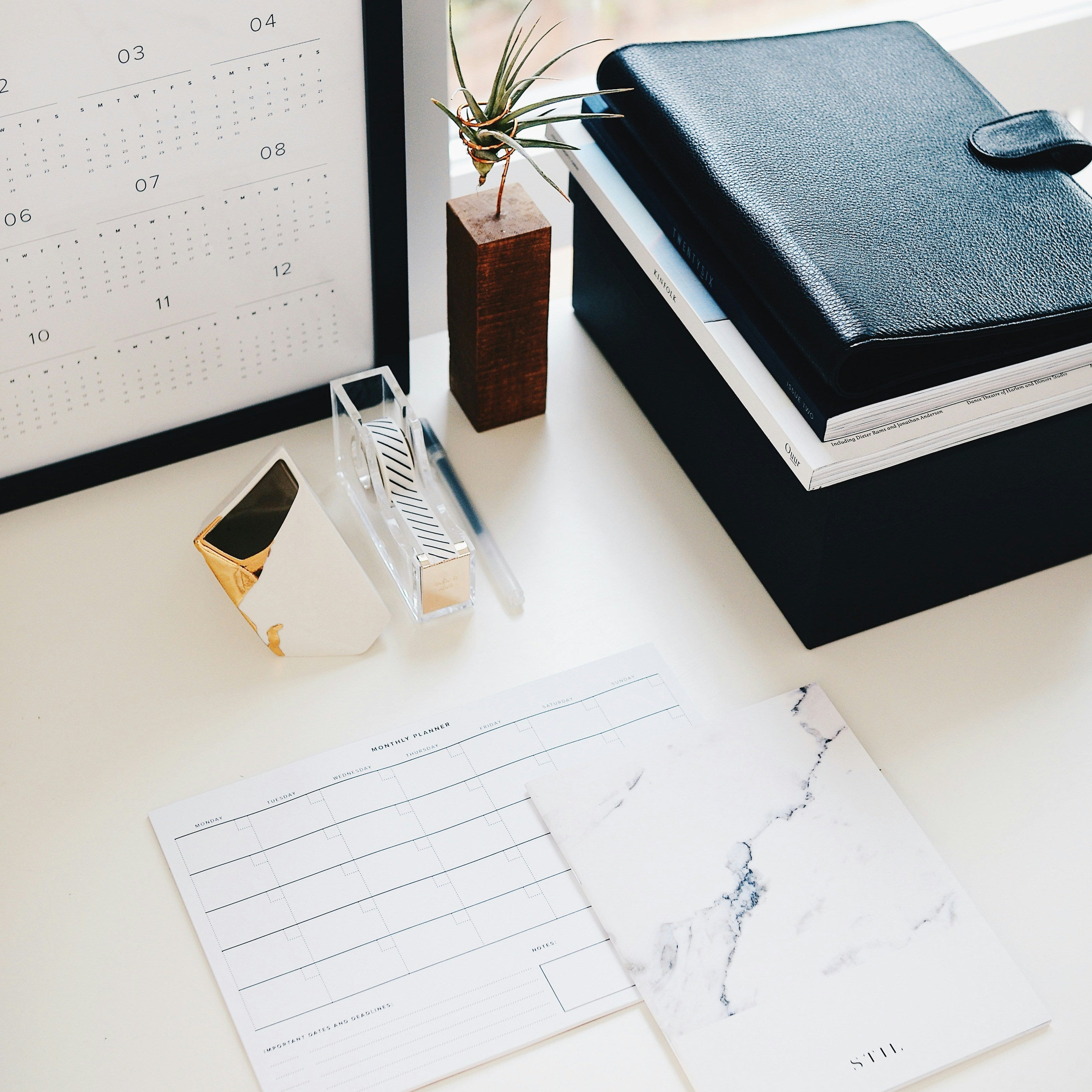 Desk setup with planner, calendar, and stationery items on a light surface.