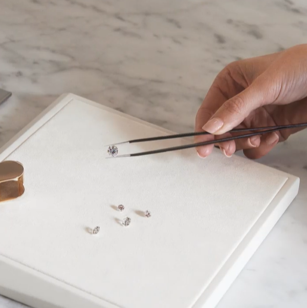 Person using tweezers to handle small jewelry pieces on a marble surface