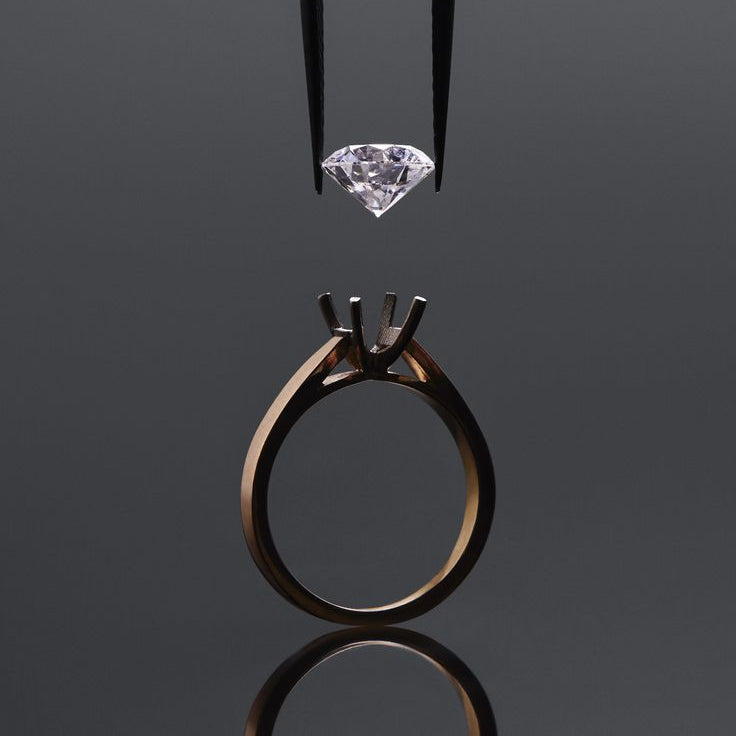Diamond hold by tweezers and rose gold ring on a reflective black surface