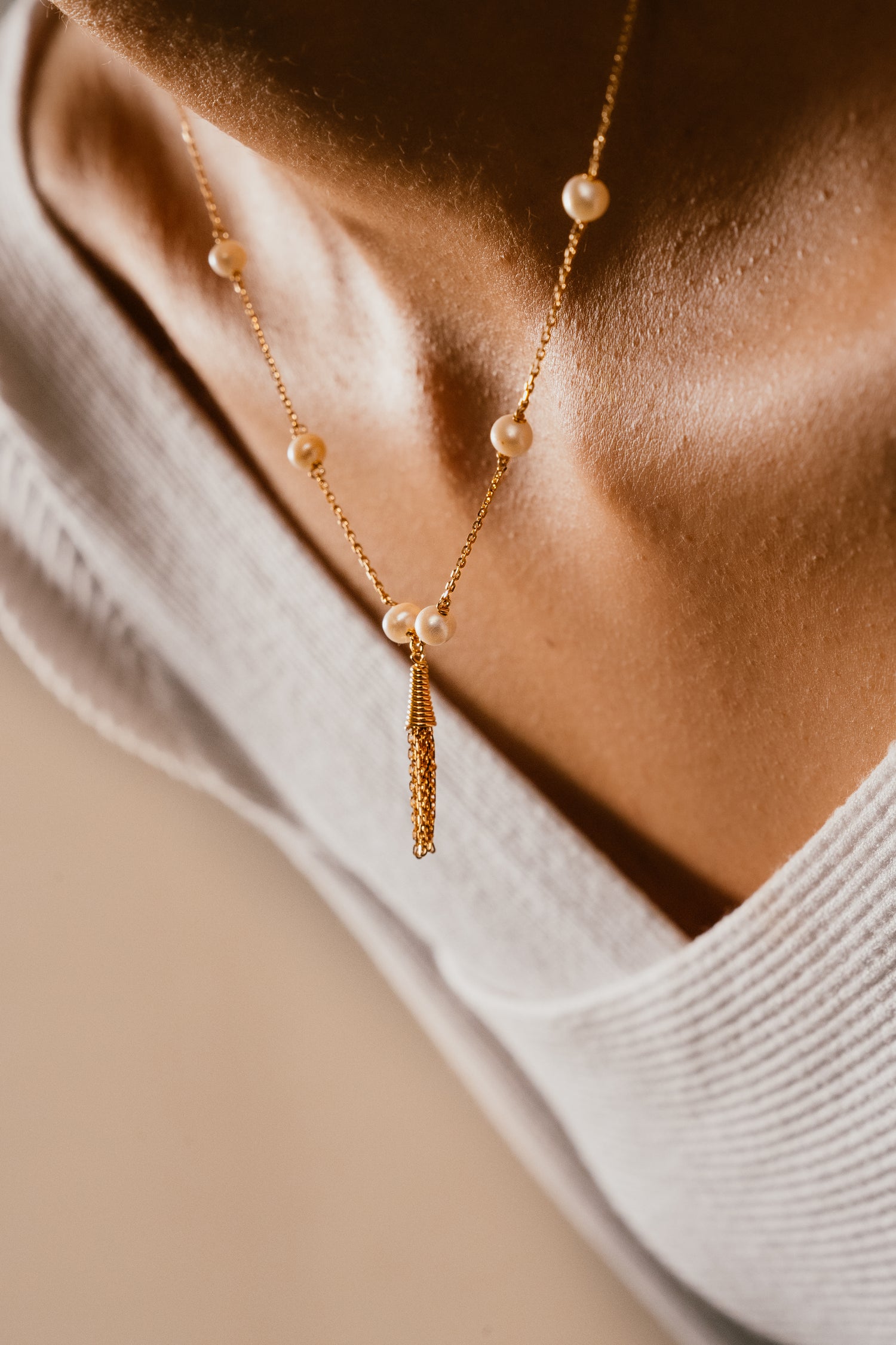 Gold necklace with pearls worn by a person, close-up on skin and clothing.