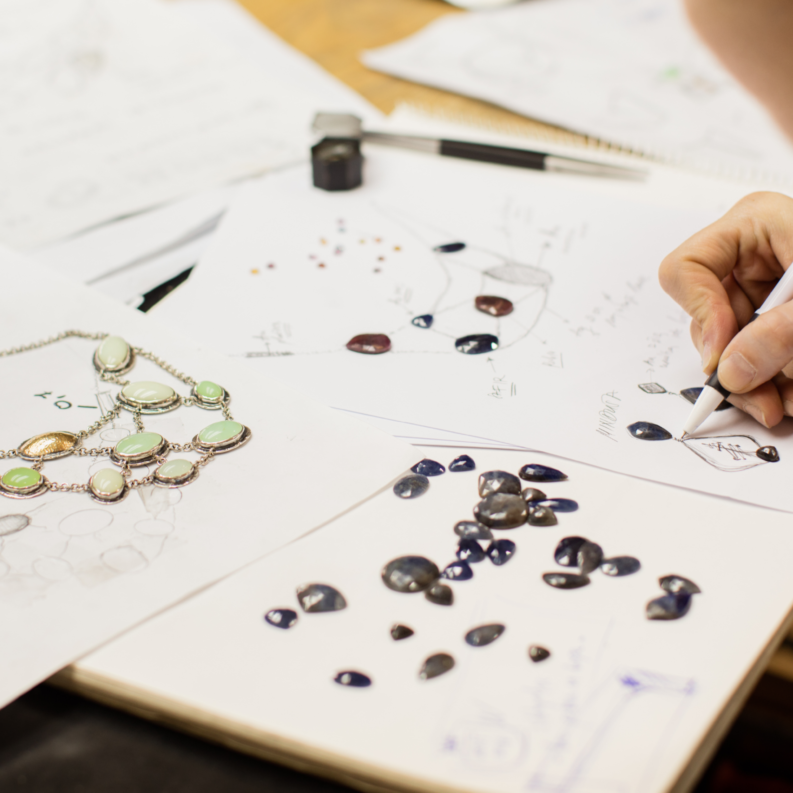 Person drawing jewelry designs on paper with colored stones