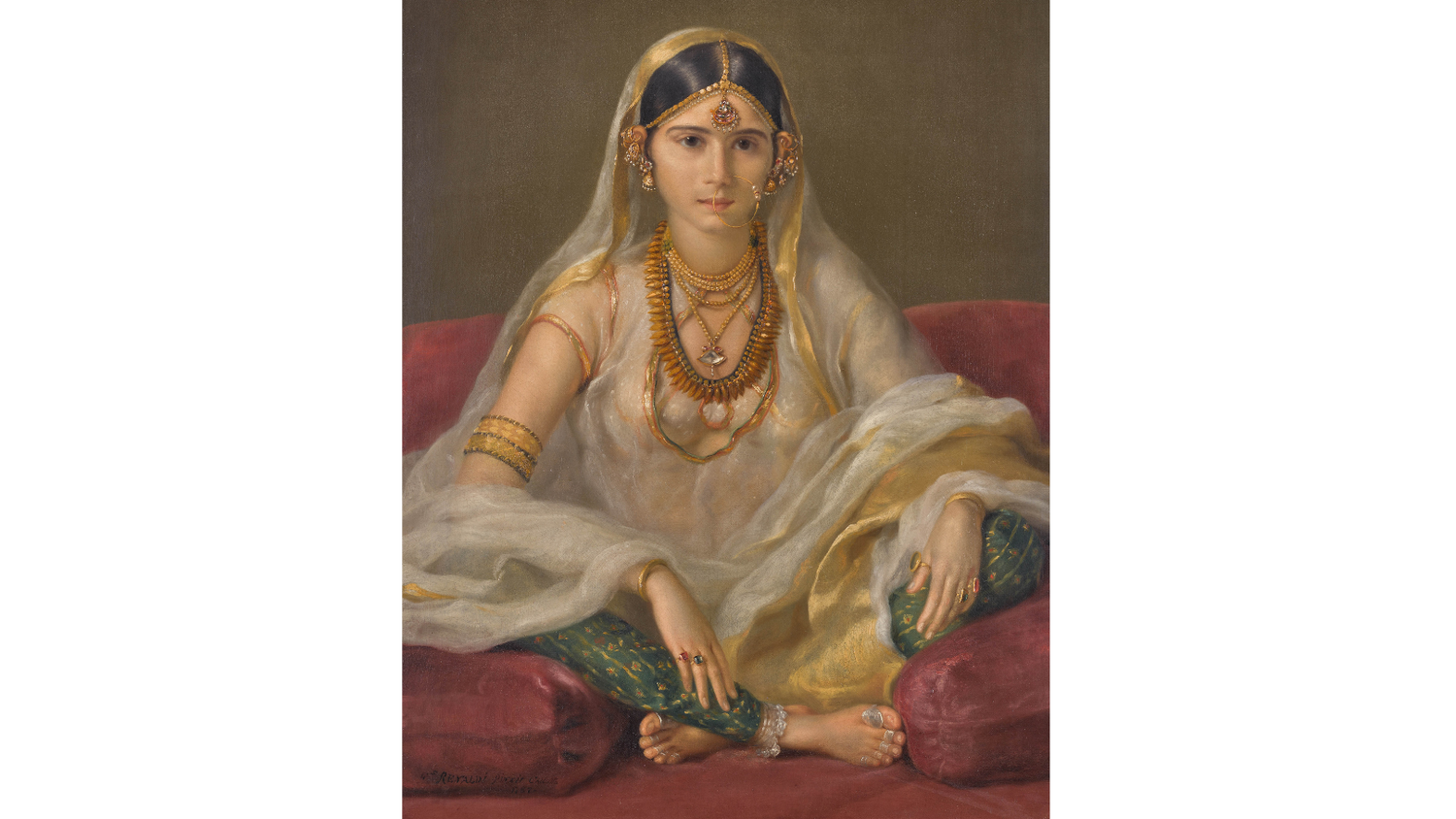 Portrait of a woman in Indian traditional attire with jewelry, sitting on a red cushion.