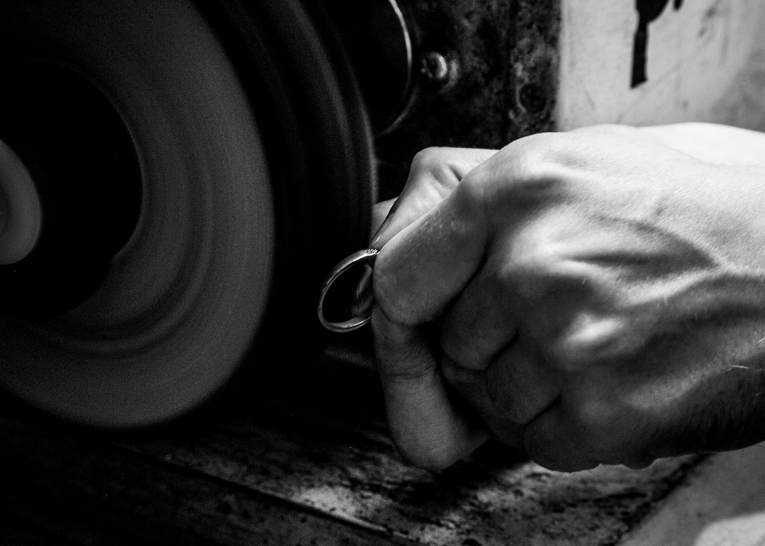 Hand holding a ringt near a polishing wheel in a workshop setting