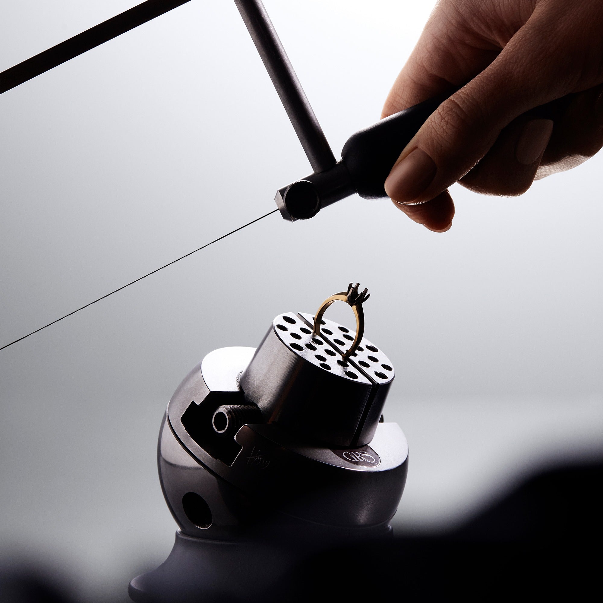 Person using a saw blade on a gold ring on a reflective surface.