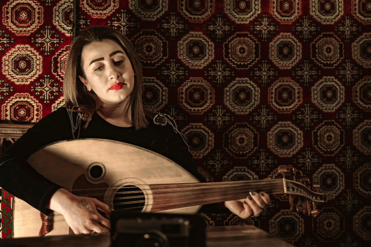 Woman playing a oud against a patterned wall.