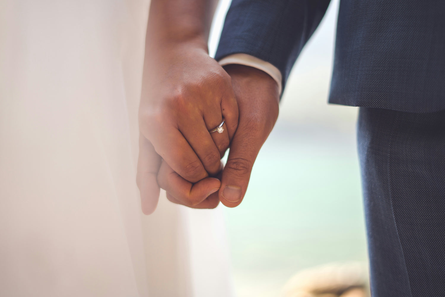 Bride and groom holding hands with the bride wearing an engagement ring in platinum and diamond.