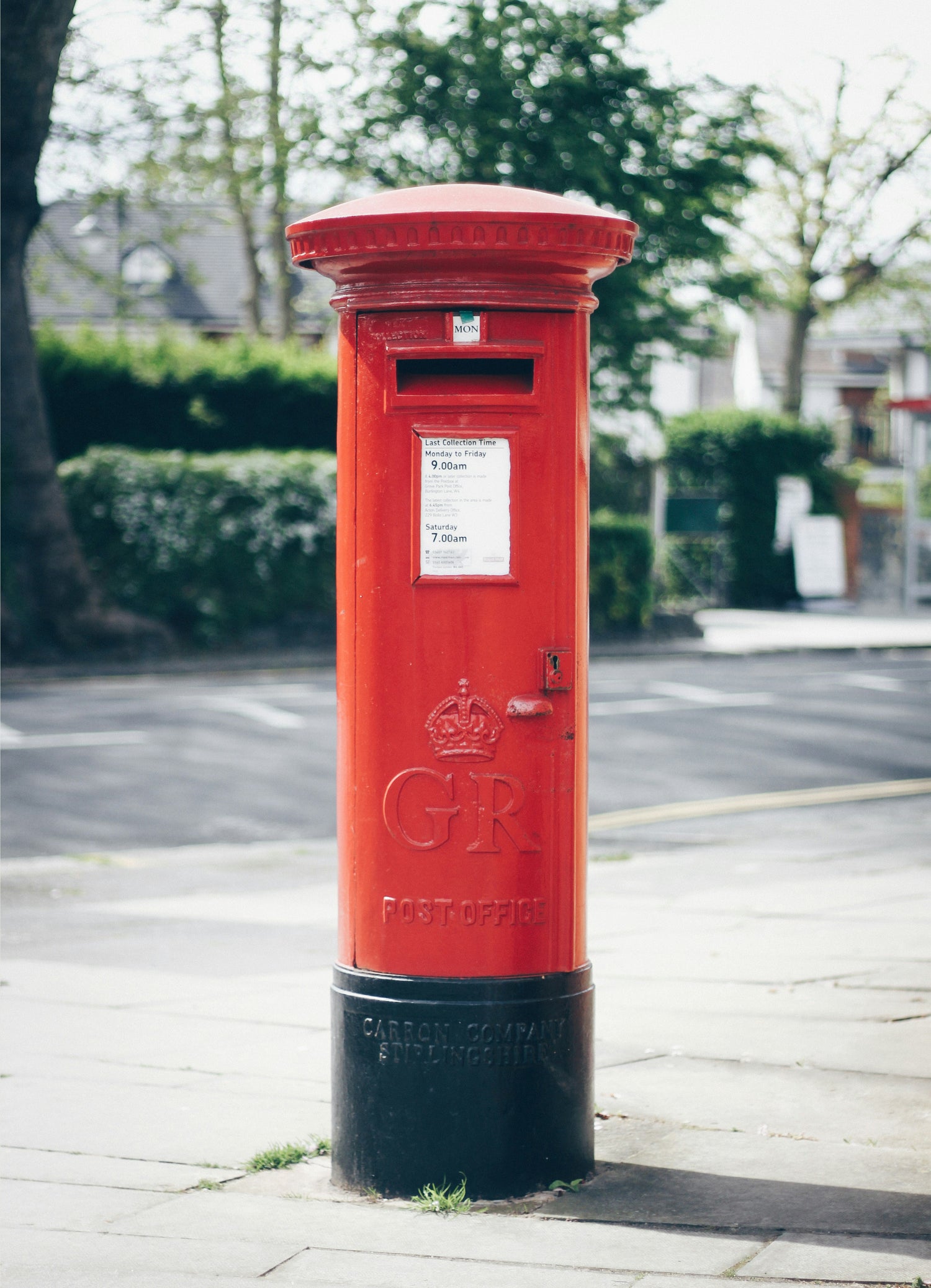 Red British postbox on a street with greenery in the background