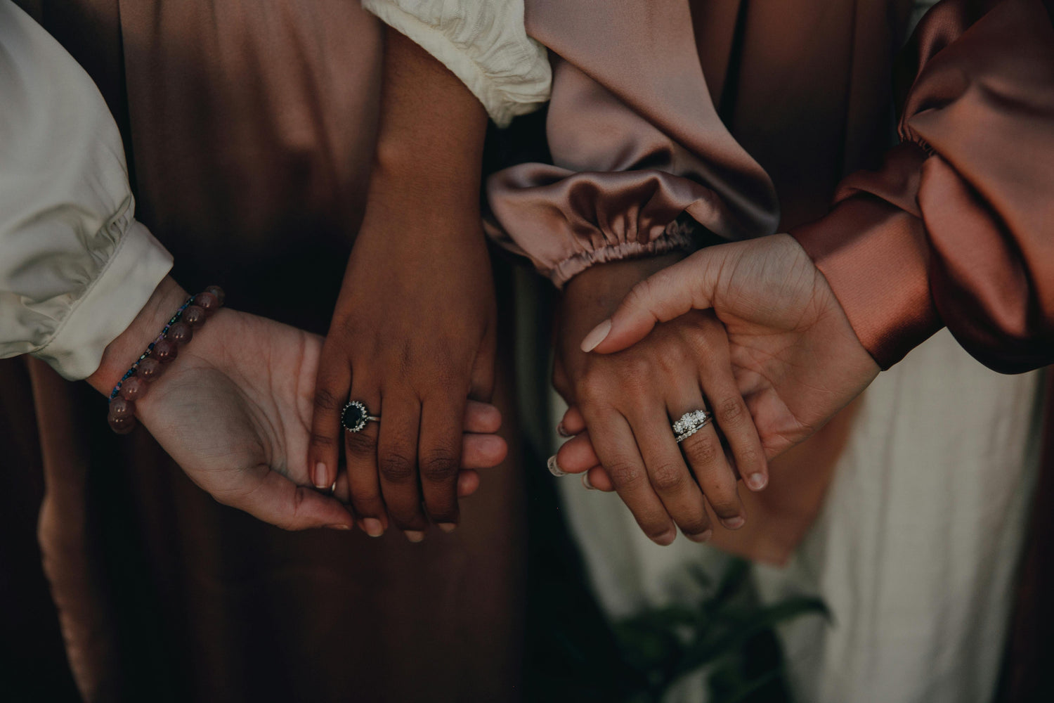 Three hands with rings held together, featuring a warm color palette.