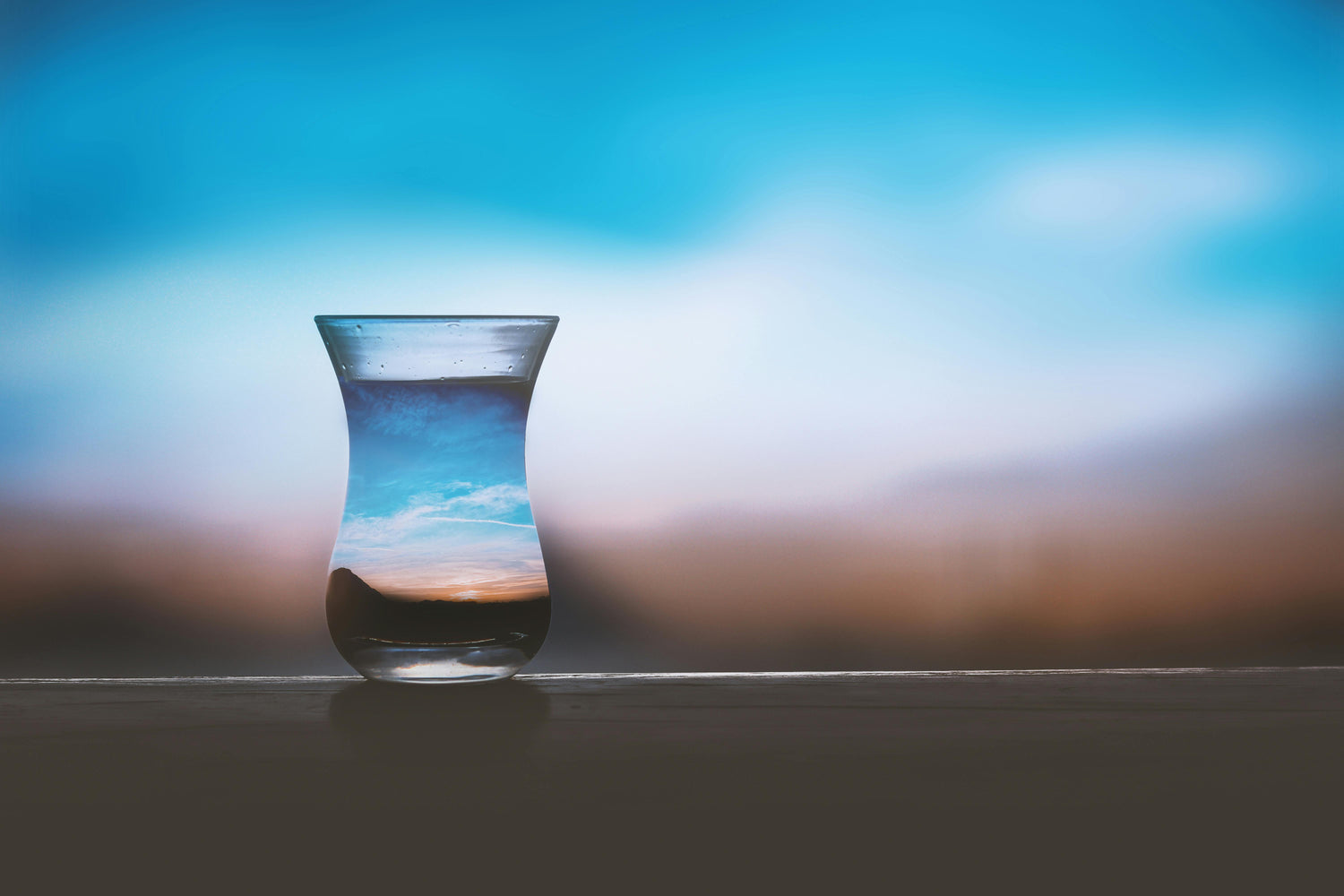 Glass with water and reflection of sky and clouds on a blurred background