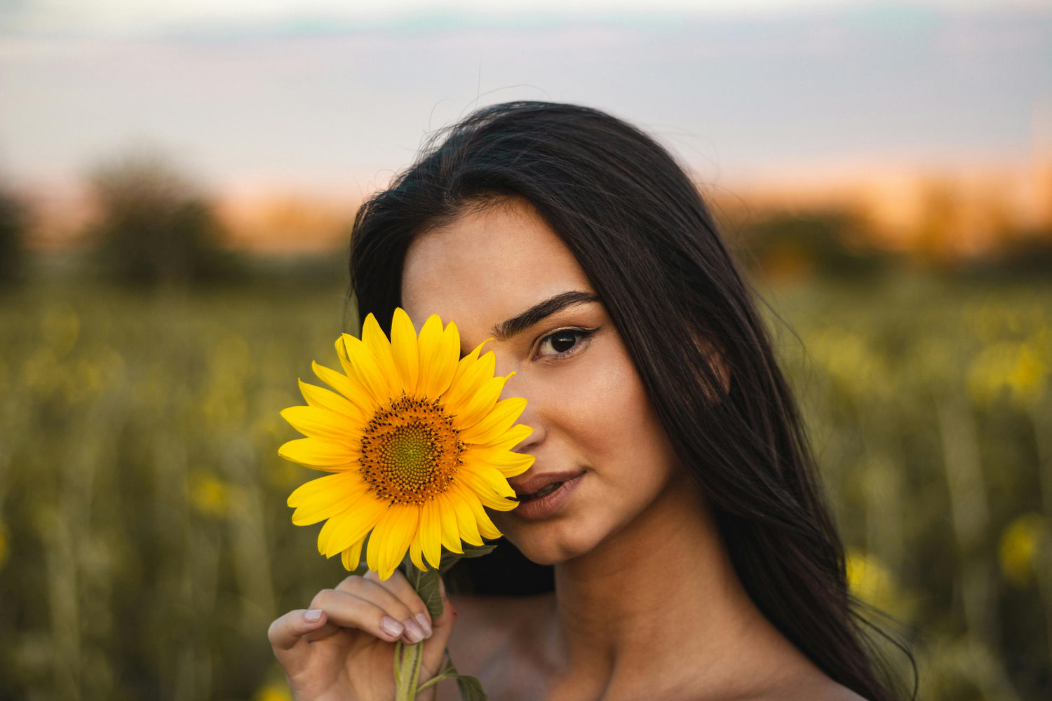 Woman holding a sunflower in a field during sunset